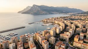 Vue aérienne réaliste de Toulon montrant le port, les immeubles résidentiels et le mont Faron sous une lumière douce.